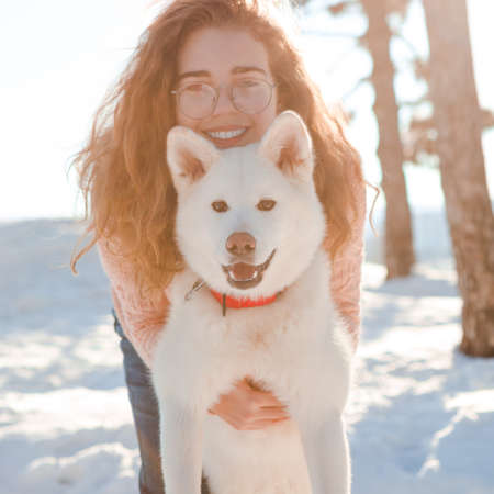 A curly-haired girl walks with a white akita in a snowy forest.の写真素材