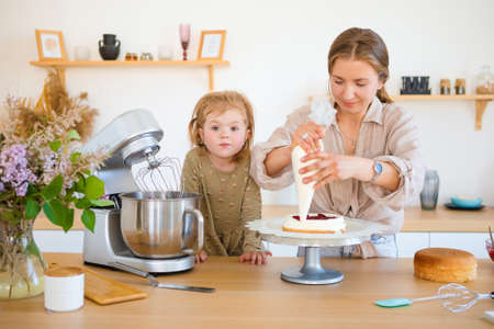 Mom and daughter are baking a beautiful dessert with cream.