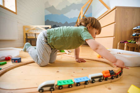 Little boy plays with a wooden railroad in a stylish nursery.の写真素材