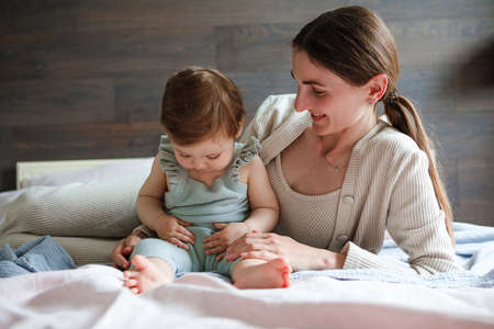 Mom plays with her little daughter in the bedroom. Gentle hugs and fun.の写真素材