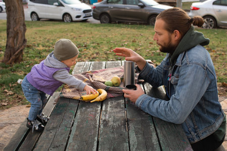 Dad and child have a picnic in the city park. Wooden table and bench.の写真素材