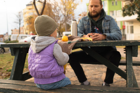 Dad and child have a picnic in the city park. Wooden table and bench.の写真素材