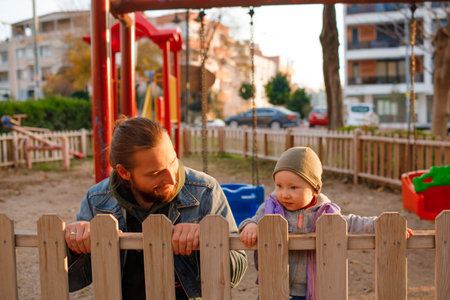 Dad and child are playing on the playground. Swing and slide rides. Sunny day.の写真素材