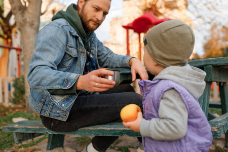 Dad and child have a picnic in the city park. Wooden table and bench.の写真素材