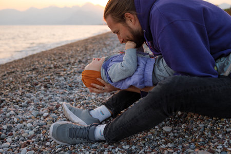 Dad and child are sitting on the beach. Warm autumn day on the Mediterranean Sea.の写真素材