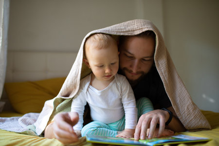 Dad with a beard and long hair reads a book to a kid. home leisure.