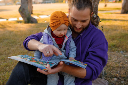 Dad and baby read a book under a tree in the park. mediterranean landscape.の写真素材