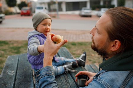 Dad and child have a picnic in the city park. Wooden table and bench.の写真素材