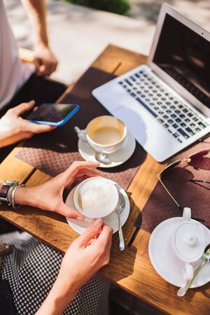 a interpreter for business meeting in a cafe. the girl is holding a coffee Cup, the man is holding a phone. there is a laptop on the tableの写真素材