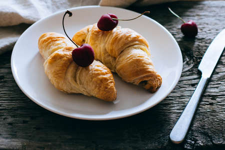 Croissants with fresh cherries, on a white plate. Wooden backgroundの写真素材