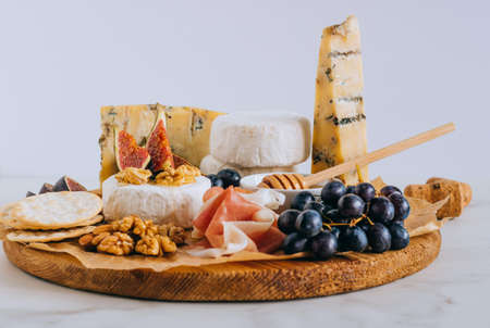 Camembert and blue cheese Stilton with figs, jamon, honey and grapes. Cheese plate on marble...