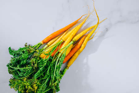Fresh washed yellow and orange carrots with a tops on a marble background, flat lay, top view