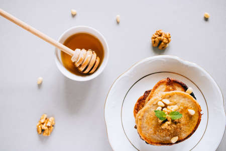 Flat lay banana pancakes with walnuts and cedar nuts, honey and mint, honey dipper on a white...