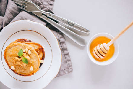 Flat lay banana pancakes with walnuts and cedar nuts, honey and mint, honey dipper on a white background, top view.の写真素材