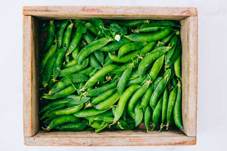Fresh peas in a wooden box on a marble background, flat lay, top view