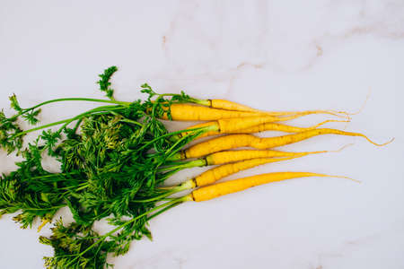 Fresh washed yellow carrots with a tops on a marble background, flat lay, top viewの写真素材