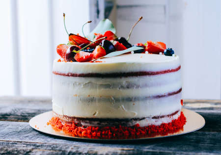 Red velvet cake with berry decoration made from strawberry, blueberry, cherry and eucalyptus on a wooden backgroundの写真素材