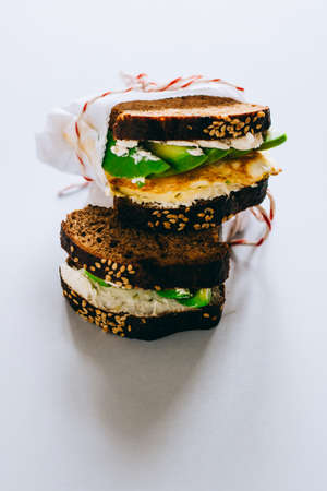 A useful sandwich with avocado and egg, wrapped in white paper with a tiny whisk on a white background.の写真素材