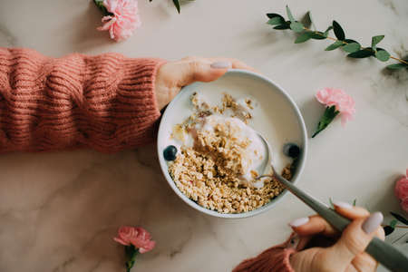 Woman in coral woolen sweater eating breakfast bowl with muesli and yogurt, berries and hazelnuts. Clean eating, vegetarian, vegan, alkiline diet food conceptの写真素材