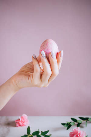 The girl is holding in hand a pink easter egg, pink and marble background, minimalism, flowersの写真素材