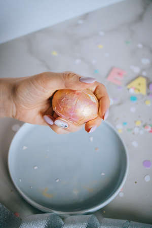 Girl breaks golden easter eggs on marble background, confetti, sparkles, ribbons.