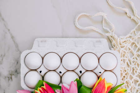 Easter concept, flat lay chicken eggs and colorful tulips, eco bag on marble background. Top view.