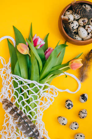 Easter concept. Spring bouquet of multicolored tulips in eco bag with and quail eggs and feathers on...
