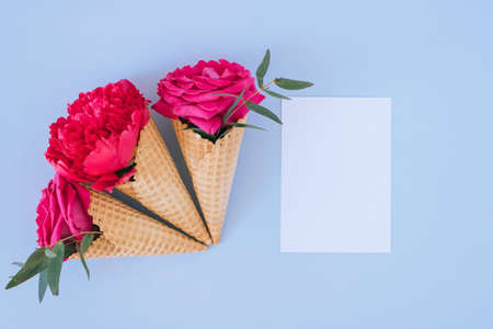 Flat lay Ice Cream Cones with pink peony and roses and white clear blank for text on blue...