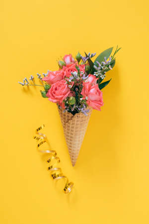 Flat lay Ice Cream Cone with colorful bouquet on yellow background, copy spaceの写真素材