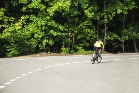lone cyclist on the road near the forest on a summer day. This is his single practice. Photo taken at t the outskirts of Moscow close to woodland Pokrovskoye-Streshnevo.の写真素材