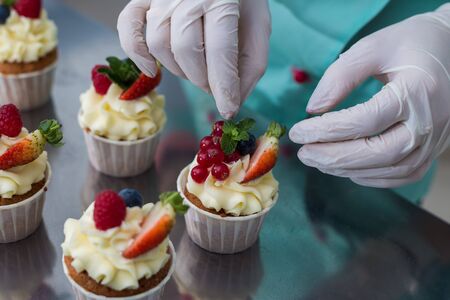 Confectioner decorate cupcakes with cream cheese and berries, close up.