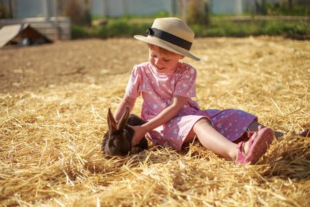 Little girl playing with rabbits on a sunny summer or spring day at sunset.の写真素材