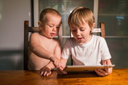 Brother and sister using digital tabletin the kitchen and watching cartoons.の写真素材