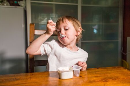 Adorable baby girl eating cottage cheese from spoon, healthy milk snack.の写真素材