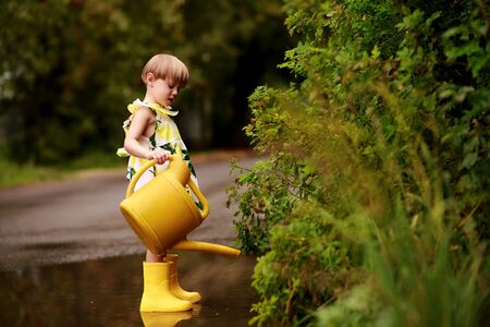Little blond girl in a colorful dress with a yellow watering can smilingの写真素材