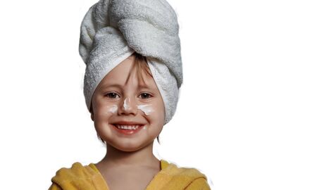 Cute girl in a yellow bathrobe with white cream on her cheeksの写真素材