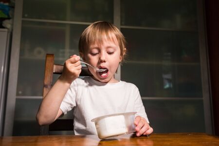 Adorable baby girl eating cottage cheese from spoon, healthy milk snack.の写真素材