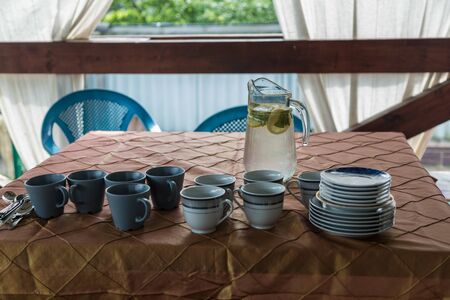 A jug with lemonade and glasses around on a table on a wooden porchの写真素材