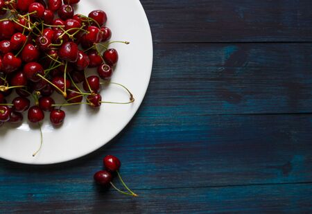Fresh cherry on plate on wooden blue background.