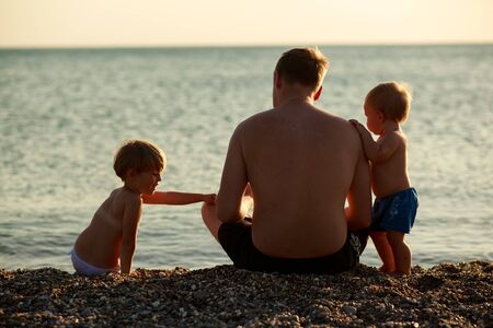 Happy family spend time together sitting on a pebble beach at sunset.の写真素材