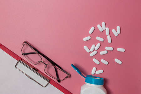 Bottle of pills near stethoscope in folder laying isolated on pink backgroundの写真素材