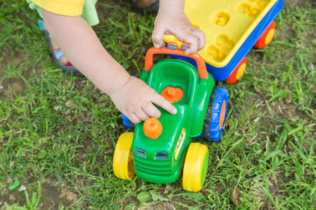 Hands of little boy with a toy tractor on the lawn of his house on a summer day.の写真素材