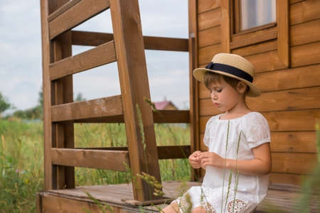 Little girl in a white boho dress and a hat against the background of a house.の写真素材
