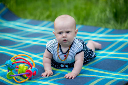 Portrait of a 6 month old baby on a plaid on the lawn with a funny mug