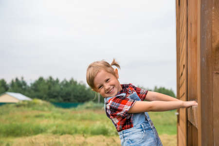 Cute little girl dressed in a denim shorts red white shirt standing on a fenceの写真素材