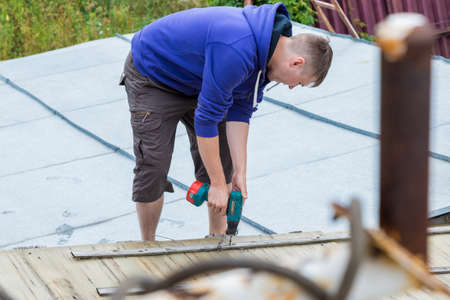 A man holds a screwdriver in his hands while standing on the roofの写真素材