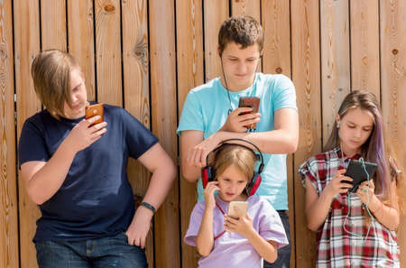 Row of four friends using cellular phones. Children and gadget concept.