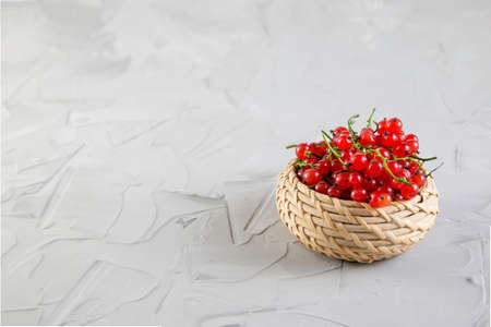 Ripe tasty bright red currants in a wicker basket on a gray concrete background.の写真素材