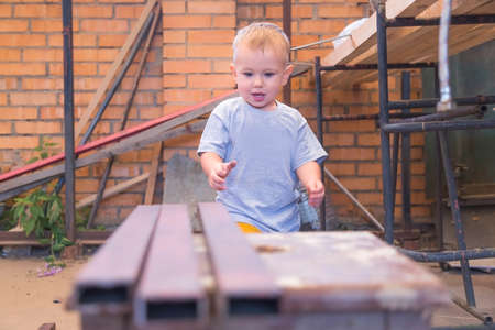 Boy is playing with iron building materials near the garage while parents don't see him. Renovation and construction at home. He wants to help his father.の写真素材