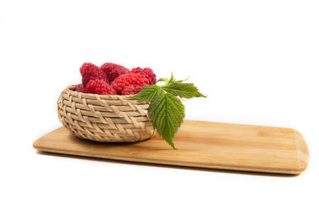 Ripe tasty bright Fresh raspberry in a wicker basket on a cutting board on a white background. High...